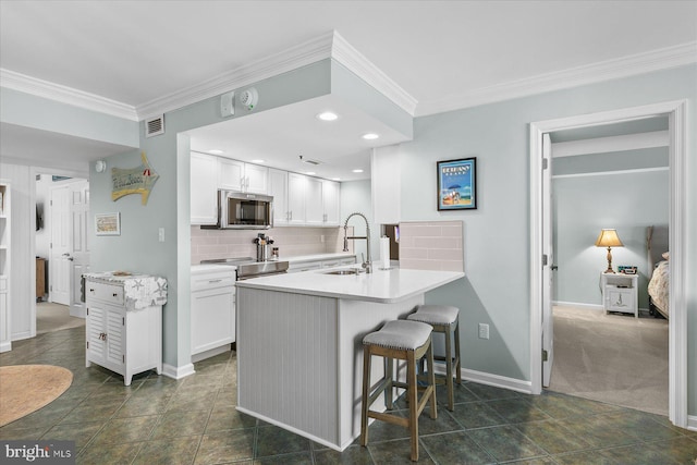 kitchen featuring a kitchen bar, white cabinetry, stainless steel appliances, decorative backsplash, and kitchen peninsula