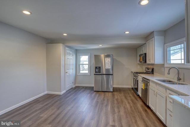 kitchen with appliances with stainless steel finishes, a healthy amount of sunlight, light stone countertops, white cabinets, and sink