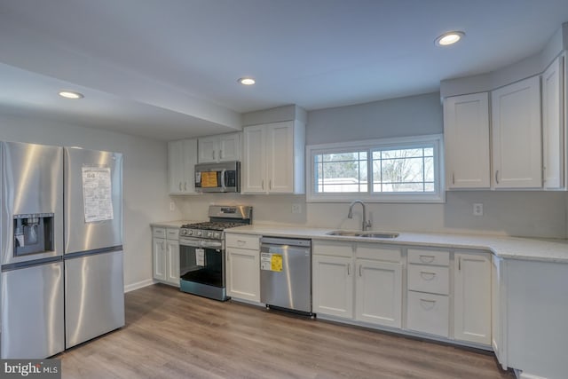 kitchen with appliances with stainless steel finishes, white cabinetry, sink, light wood-type flooring, and light stone counters