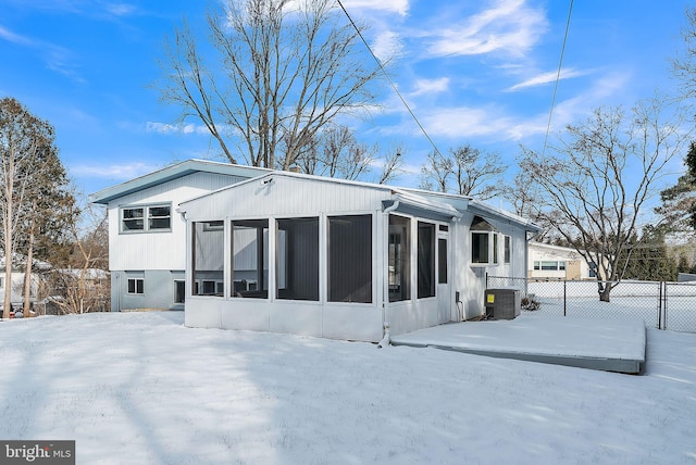 snow covered back of property featuring central AC unit and a sunroom