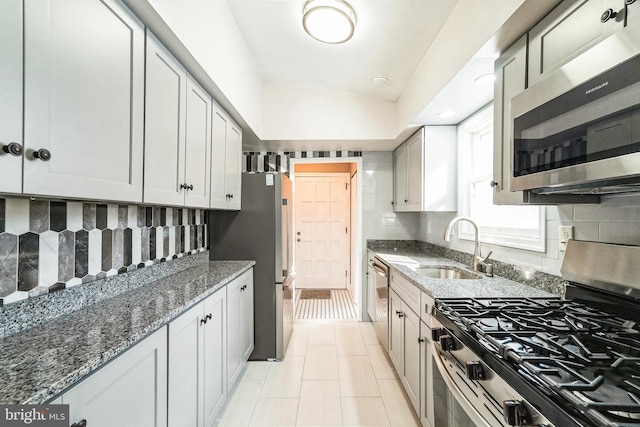 kitchen with appliances with stainless steel finishes, dark stone counters, decorative backsplash, sink, and light tile patterned floors