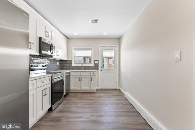 kitchen featuring light hardwood / wood-style floors, appliances with stainless steel finishes, tasteful backsplash, white cabinetry, and a baseboard heating unit