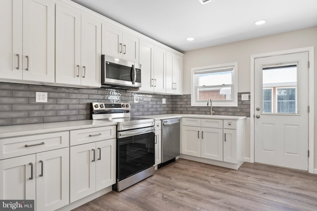 kitchen with white cabinets, light hardwood / wood-style floors, appliances with stainless steel finishes, and sink