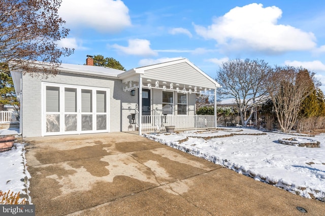 snow covered house featuring a garage and a porch