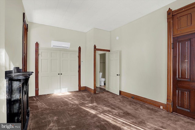 unfurnished bedroom with dark colored carpet, ensuite bathroom, and an AC wall unit