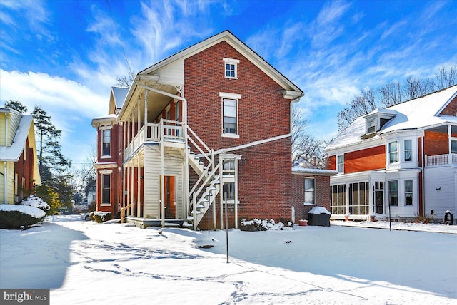 snow covered rear of property featuring a sunroom