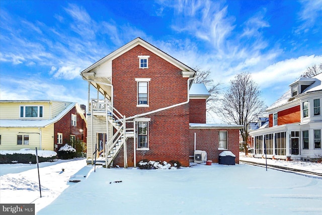 snow covered back of property with a sunroom