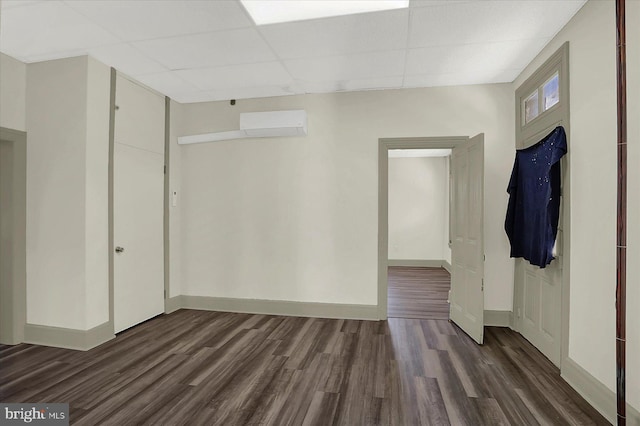 empty room featuring dark wood-type flooring, a wall mounted air conditioner, and a drop ceiling