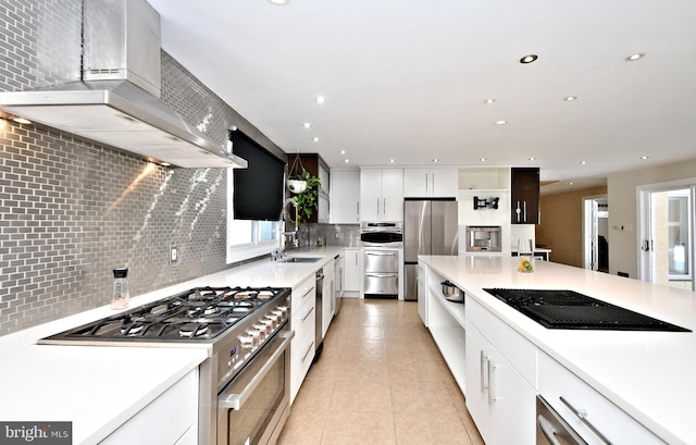 kitchen with white cabinets, backsplash, light tile patterned floors, stainless steel appliances, and wall chimney range hood