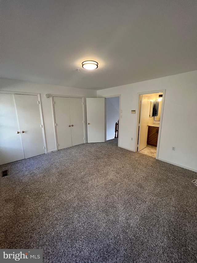 unfurnished bedroom with light colored carpet, ensuite bath, and multiple closets