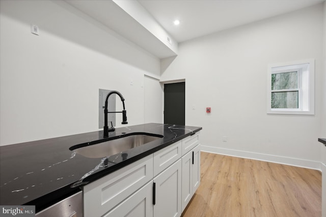 kitchen featuring light wood-type flooring, dark stone counters, sink, and white cabinetry