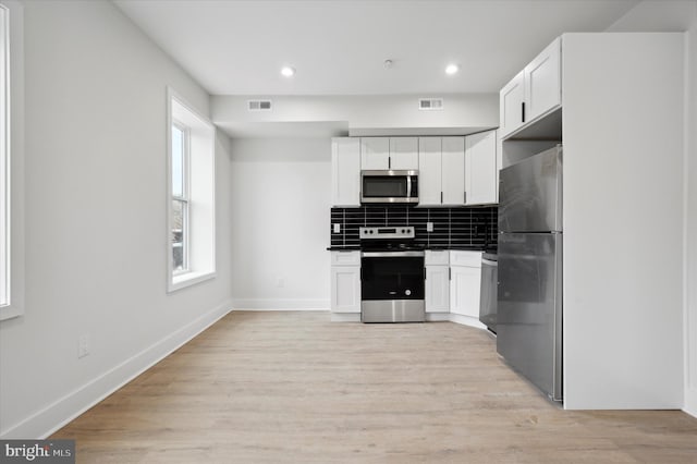 kitchen with decorative backsplash, white cabinetry, appliances with stainless steel finishes, and light hardwood / wood-style flooring