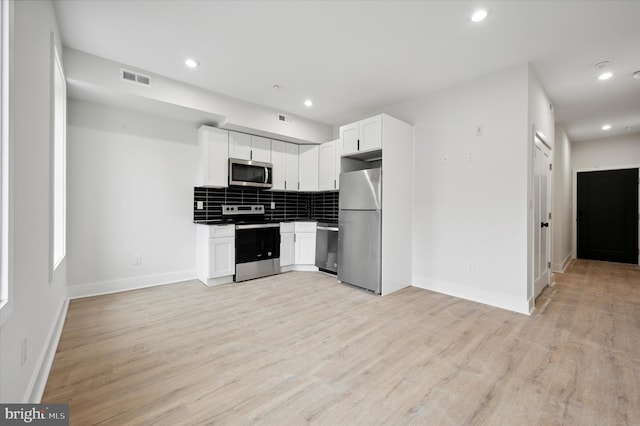 kitchen with white cabinets, appliances with stainless steel finishes, light wood-type flooring, and tasteful backsplash