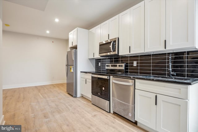 kitchen with white cabinets, stainless steel appliances, tasteful backsplash, sink, and light wood-type flooring