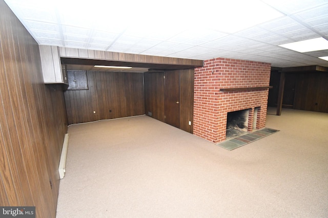 basement featuring light carpet, a fireplace, wooden walls, and a baseboard radiator