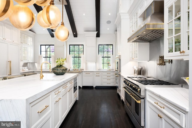 kitchen with stainless steel appliances, decorative light fixtures, wall chimney exhaust hood, white cabinets, and beamed ceiling