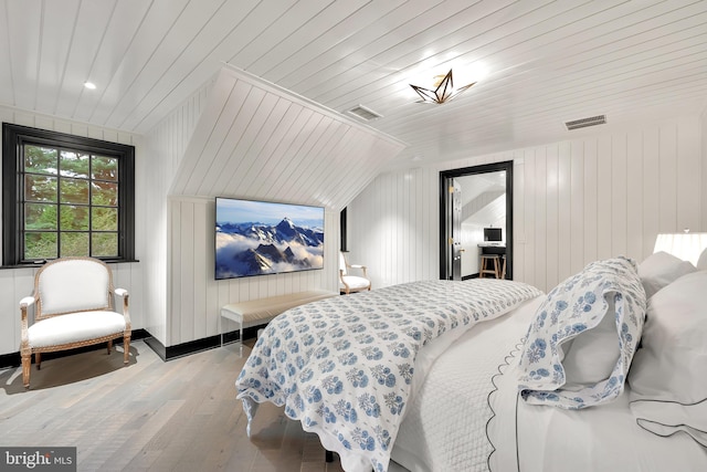 bedroom with wooden ceiling, vaulted ceiling, wooden walls, and light hardwood / wood-style floors