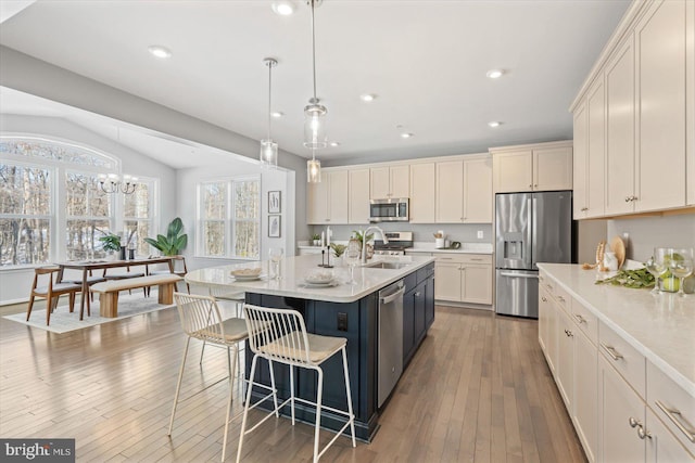 kitchen featuring pendant lighting, hardwood / wood-style flooring, stainless steel appliances, an island with sink, and vaulted ceiling