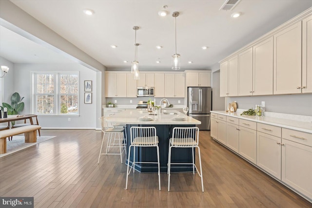 kitchen featuring sink, a center island with sink, dark hardwood / wood-style floors, pendant lighting, and stainless steel appliances