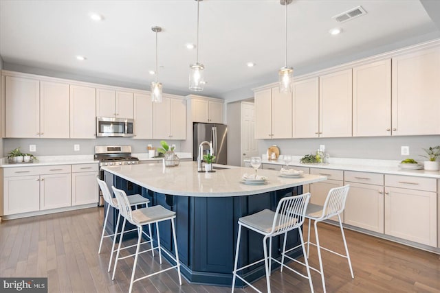 kitchen featuring decorative light fixtures, appliances with stainless steel finishes, a kitchen breakfast bar, hardwood / wood-style flooring, and a kitchen island with sink