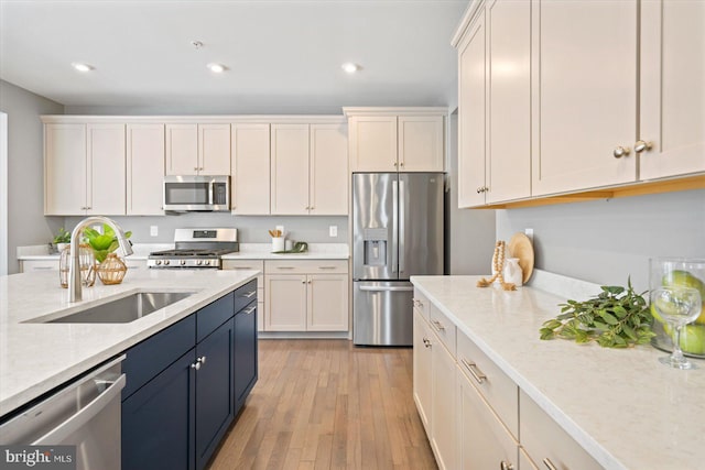 kitchen featuring stainless steel appliances, white cabinetry, sink, and light stone counters