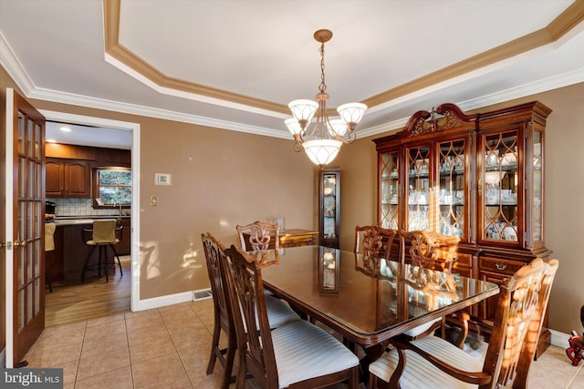 tiled dining room with crown molding, a raised ceiling, and a chandelier