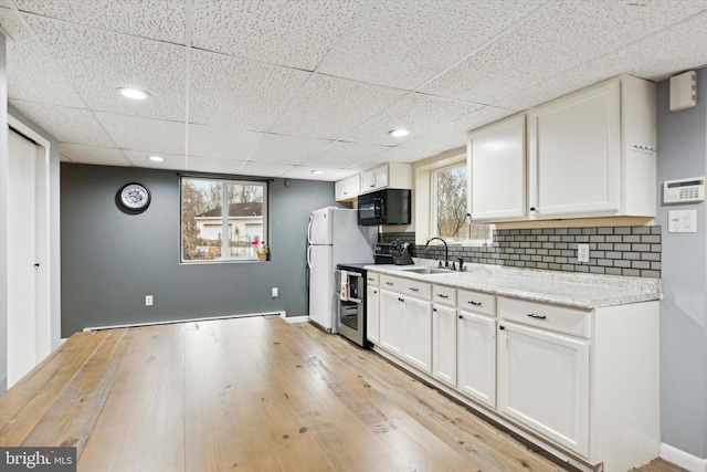 kitchen with white cabinets, range with two ovens, decorative backsplash, sink, and light wood-type flooring