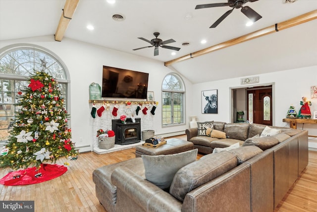 living room featuring ceiling fan, a baseboard heating unit, vaulted ceiling with beams, light hardwood / wood-style flooring, and a wood stove