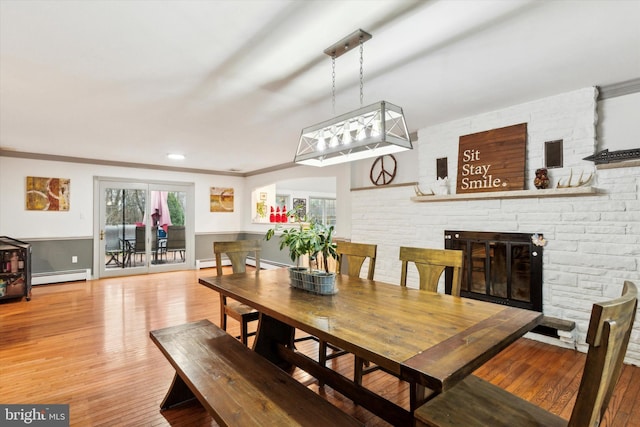 dining space with baseboard heating, a fireplace, ornamental molding, and light hardwood / wood-style flooring