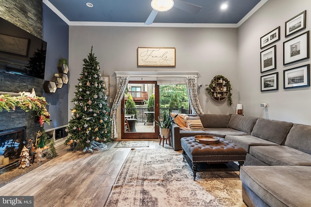 living room with ceiling fan, wood-type flooring, a stone fireplace, and ornamental molding