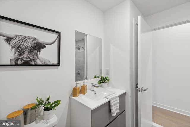 bathroom with toilet, tiled shower, hardwood / wood-style floors, and vanity