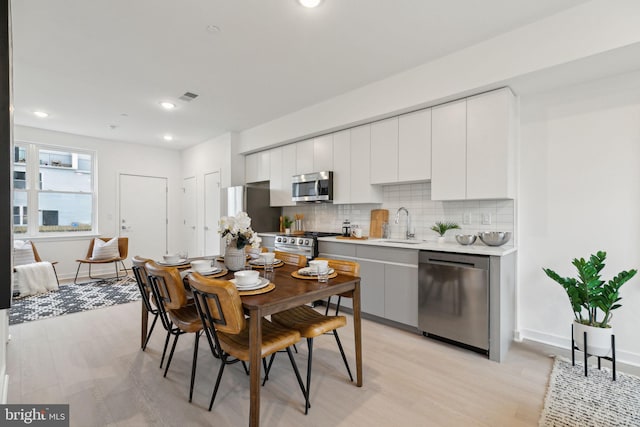 kitchen with white cabinetry, appliances with stainless steel finishes, tasteful backsplash, light wood-type flooring, and sink