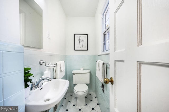 half bathroom featuring tile patterned flooring, toilet, a sink, tile walls, and wainscoting