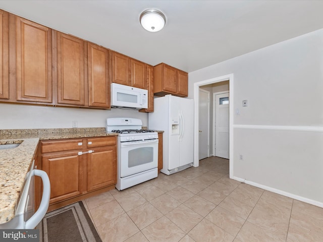 kitchen with light stone counters, white appliances, light tile patterned flooring, and sink