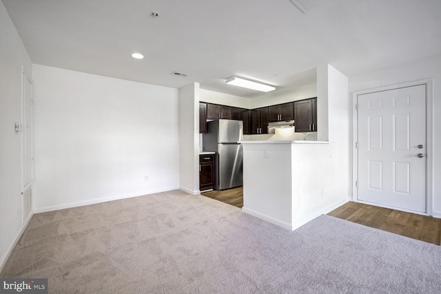 kitchen with carpet floors, stainless steel fridge, dark brown cabinetry, and kitchen peninsula