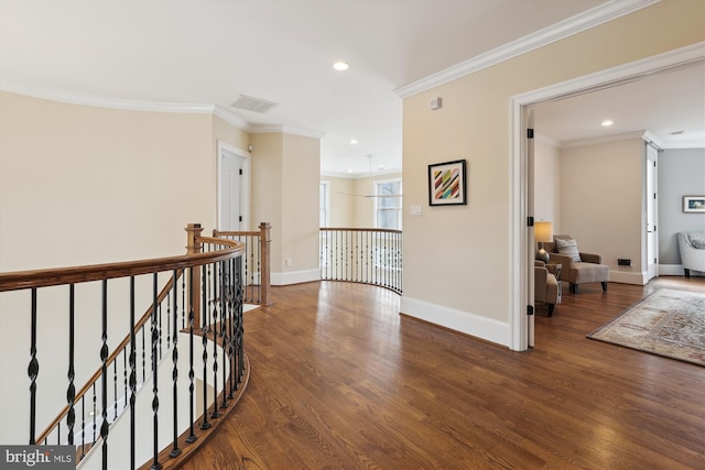 hall featuring baseboards, visible vents, wood finished floors, crown molding, and an upstairs landing