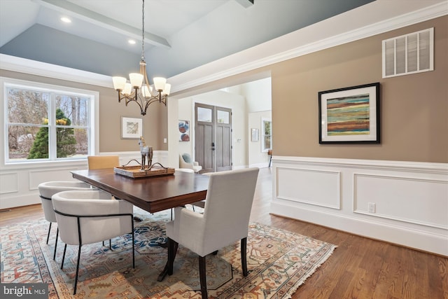 dining room featuring a notable chandelier, wood finished floors, visible vents, ornamental molding, and wainscoting