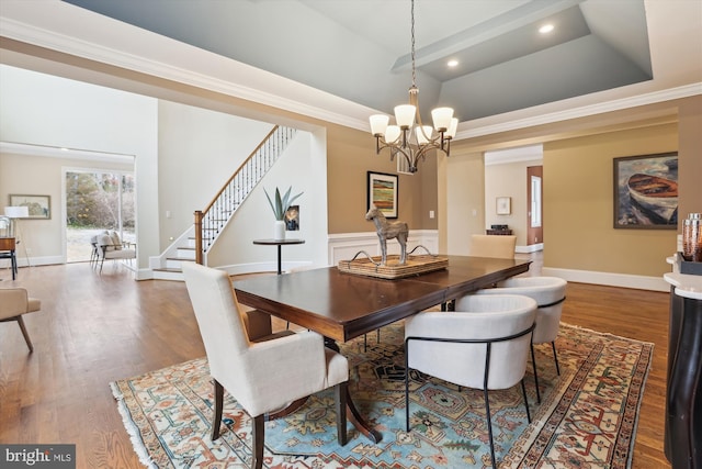 dining space featuring a chandelier, wood finished floors, stairs, ornamental molding, and a raised ceiling