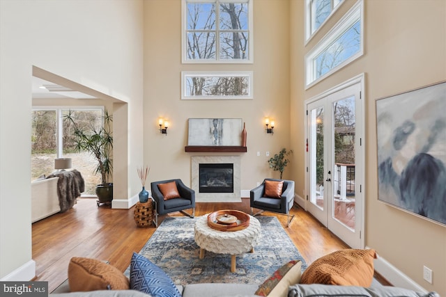 sitting room with light wood-type flooring, a glass covered fireplace, plenty of natural light, and baseboards