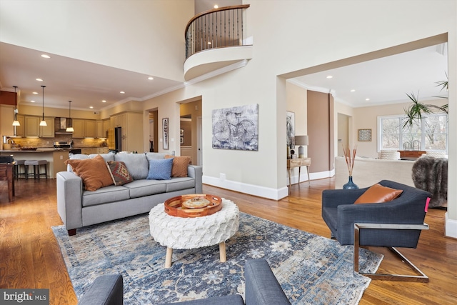 living area featuring light wood finished floors, baseboards, a towering ceiling, ornamental molding, and recessed lighting