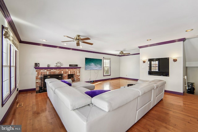 living room with a brick fireplace, wood-type flooring, ornamental molding, and ceiling fan