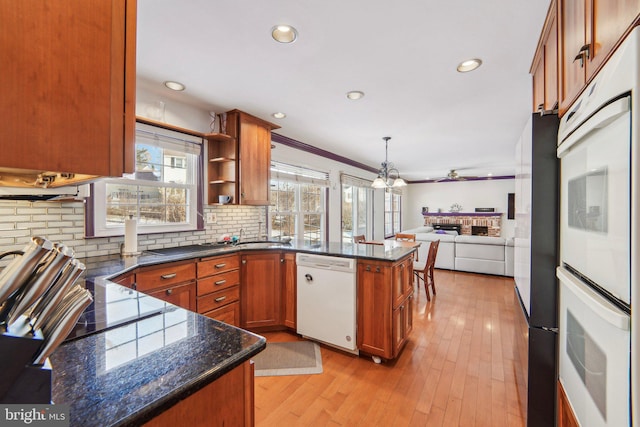 kitchen with backsplash, dark stone counters, hanging light fixtures, white dishwasher, and light wood-type flooring