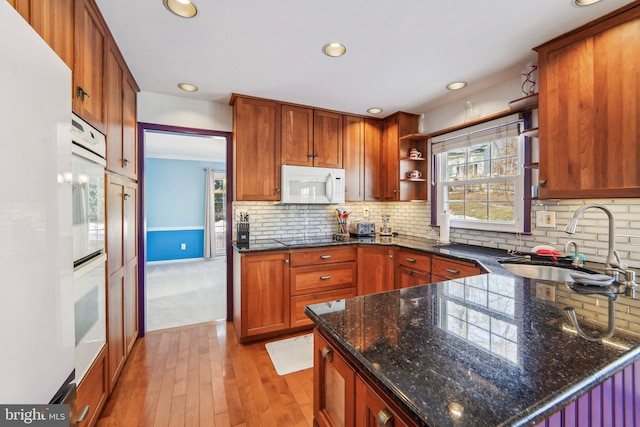 kitchen featuring sink, dark stone counters, light hardwood / wood-style floors, plenty of natural light, and white appliances