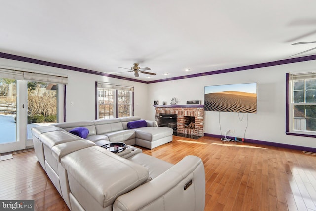 living room with crown molding, a brick fireplace, hardwood / wood-style flooring, and ceiling fan