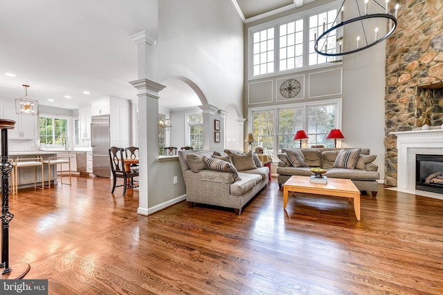 living room with a stone fireplace, sink, ornate columns, wood-type flooring, and ornamental molding