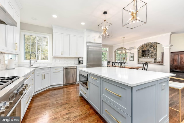 kitchen featuring sink, built in appliances, a center island, hanging light fixtures, and white cabinets