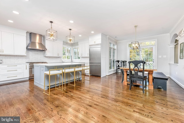 kitchen featuring white cabinetry, premium appliances, a center island, and wall chimney range hood