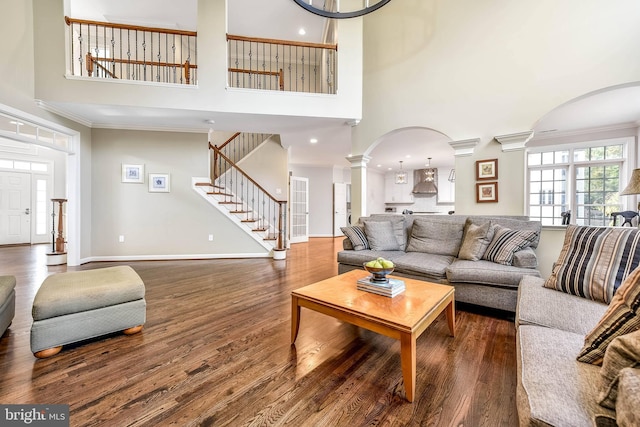 living room featuring crown molding, dark wood-type flooring, decorative columns, and a towering ceiling