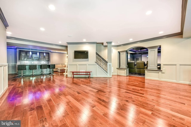 living room featuring bar area, crown molding, wood-type flooring, and ornate columns