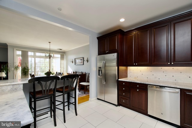 kitchen with pendant lighting, stainless steel appliances, tasteful backsplash, light stone countertops, and ornamental molding